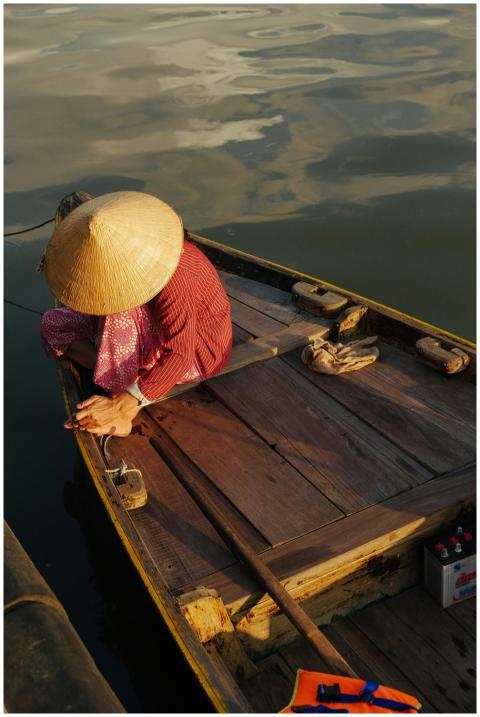 Person in a conical hat sitting on a wooden boat o