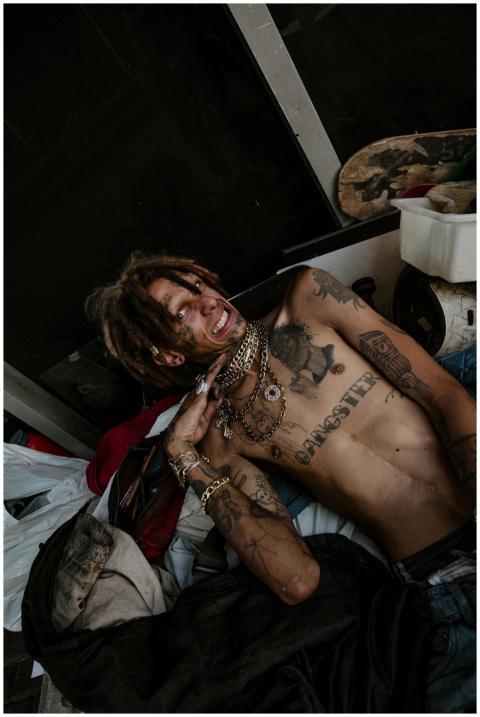 A shirtless man with tattoos and dreadlocks poses