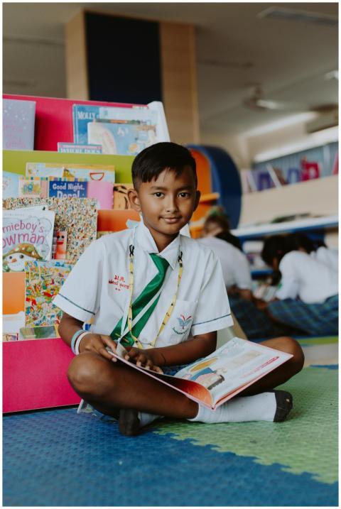 A boy in a school uniform sits cross-legged readin