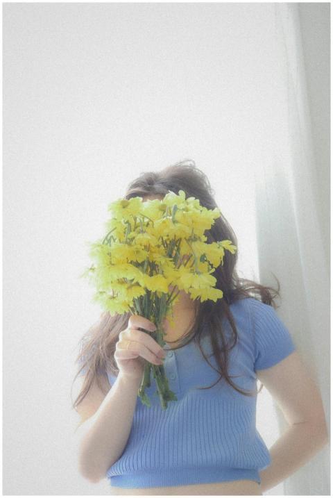 A woman in a blue top playfully hides her face wit