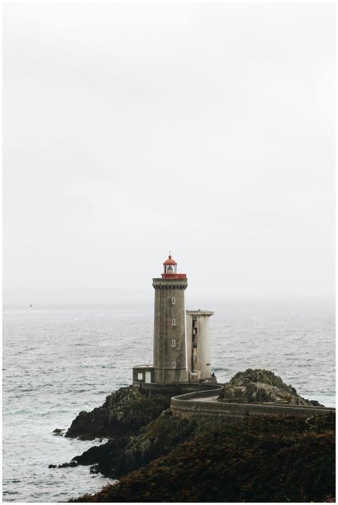 A solitary lighthouse stands on a rocky shore, ove