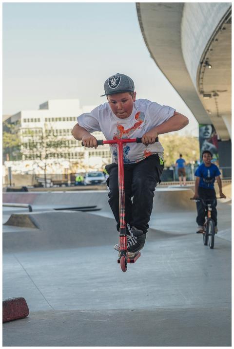 A young boy in mid-air on a scooter at an urban sk