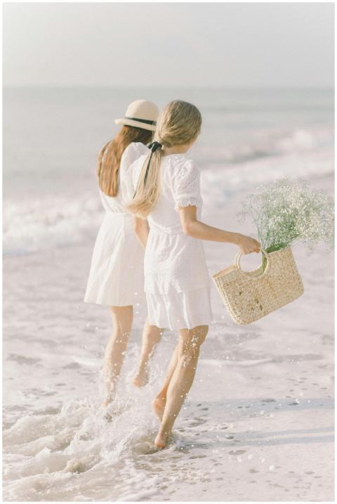 Two women in white dresses walk along a sunny beac