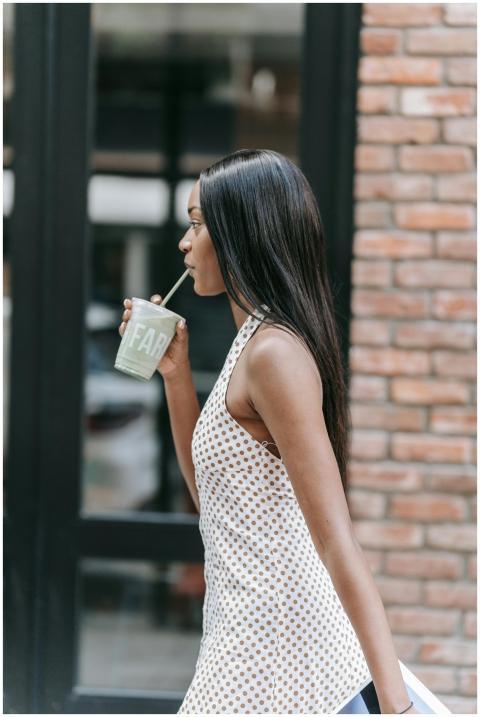A woman in a polka dot top sips from a disposable