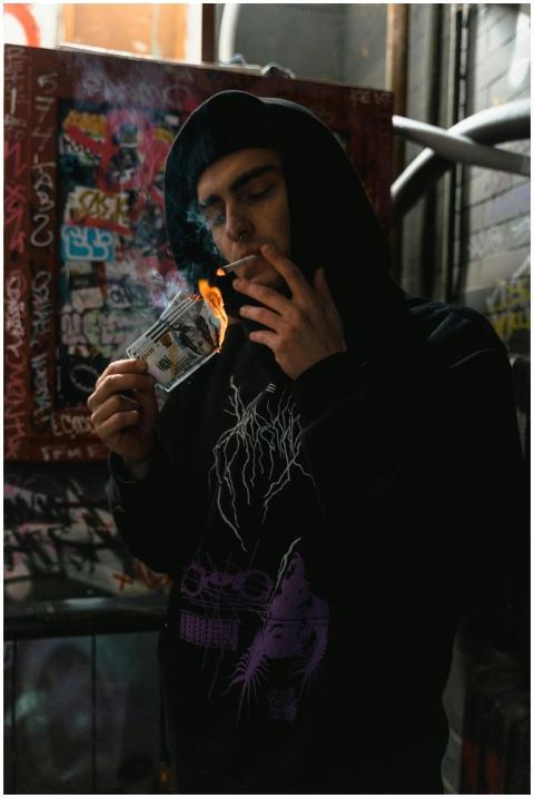 A young man in a black hoodie smokes in a graffiti