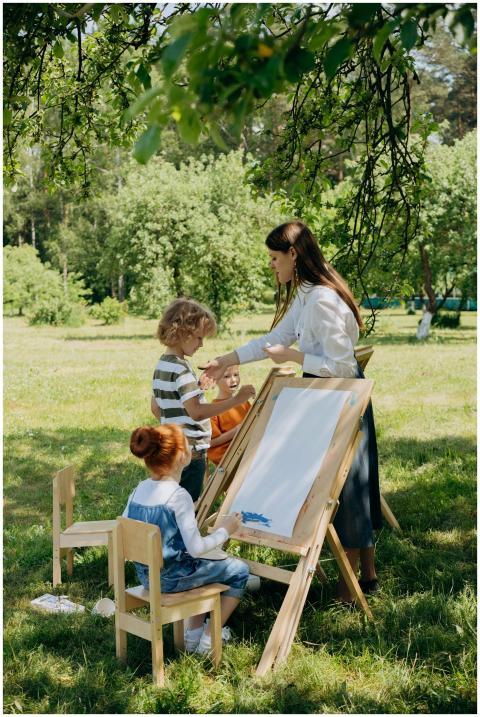 Children painting with instructor in a sunny garde