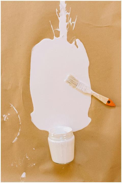 A brush beside a white paint spill on brown paper,