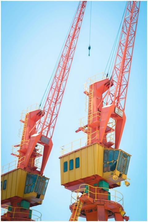 Two vibrant orange cranes under a clear blue sky,