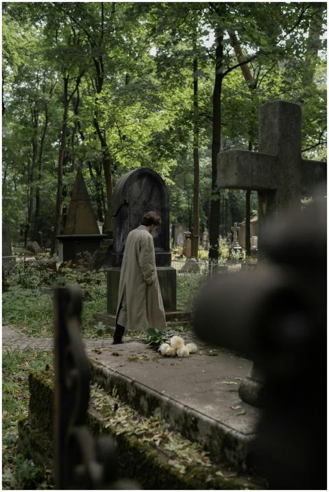 A person in a trench coat reflects in an overgrown