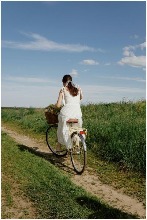 A woman in a white dress rides a bicycle along a g