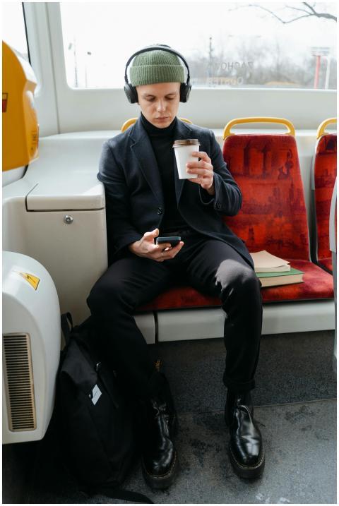 Man sitting on a bus, wearing headphones and holdi