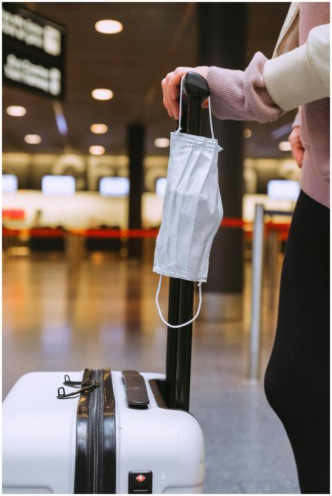 Person standing with luggage and face mask hanging