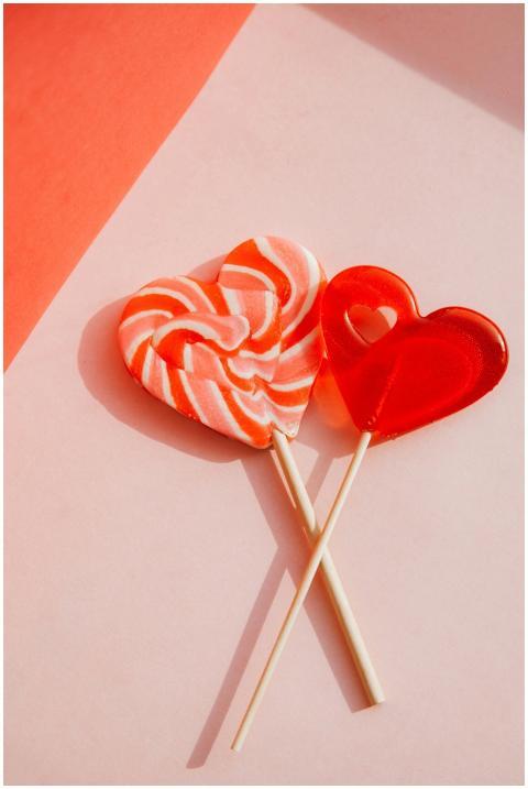Two heart-shaped lollipops on a pastel pink surfac