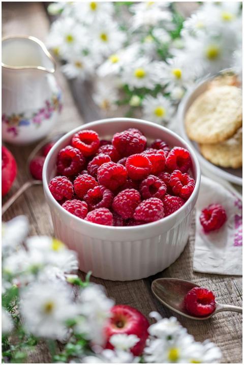 Ripe red raspberries in a bowl on a rustic table w