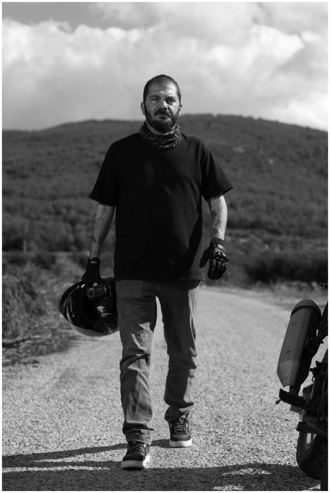 A motorcyclist walks with helmet on a gravel road,