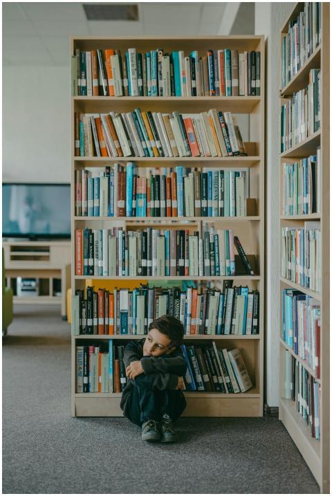 A young boy sits alone in a modern library, appear