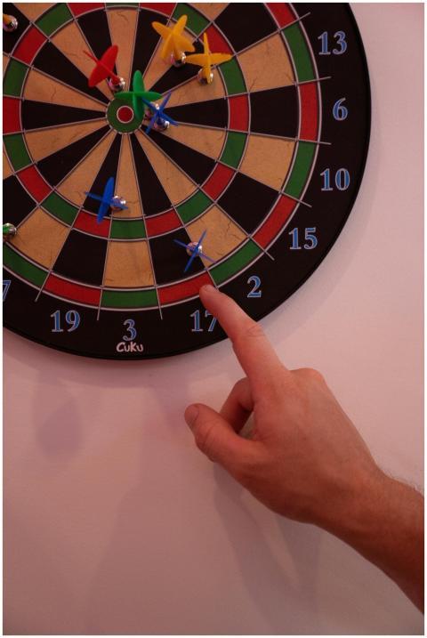 Close-up view of a dartboard with a hand pointing