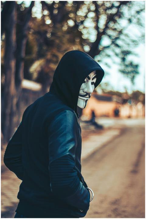 A man in a hoodie wearing a Guy Fawkes mask walks