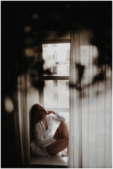 A woman sits thoughtfully by a window, bathed in s