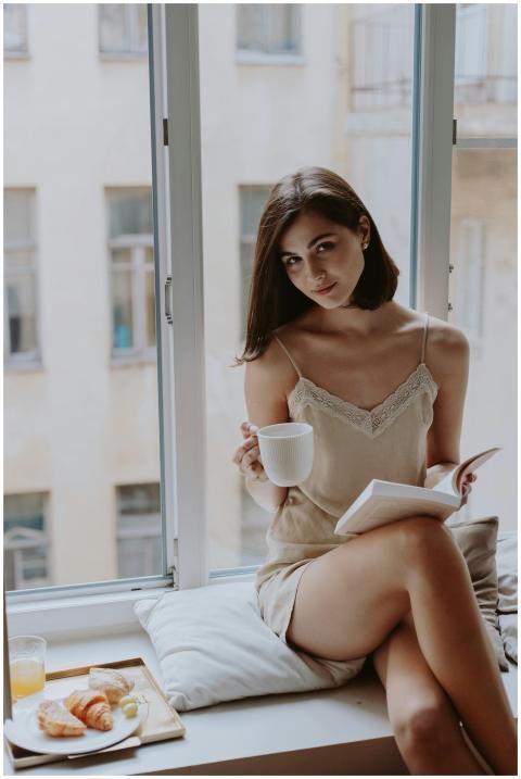 Woman sitting by window, enjoying coffee and book