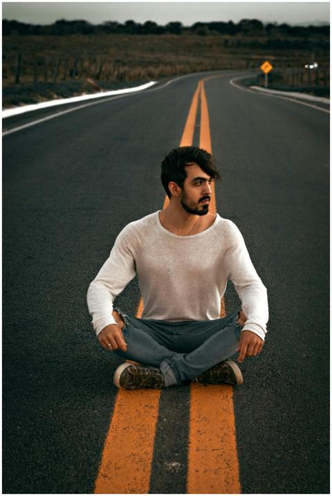 A thoughtful young man sits on an empty road, embo