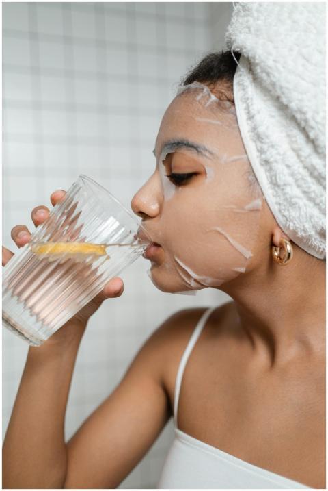 Woman in skincare routine with sheet mask, drinkin