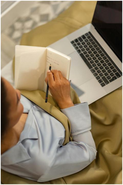 A woman sits on a bed while writing in a notebook,