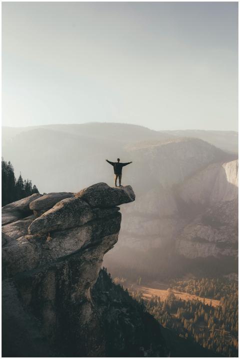 Person with arms raised standing on cliff edge, su