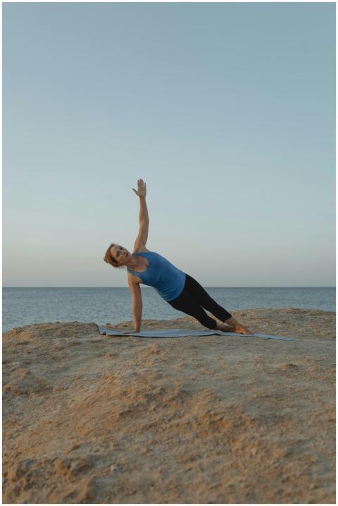 A woman performs a yoga side plank on a beach at s