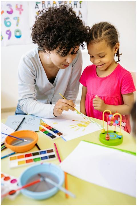 A teacher assists a child with painting, promoting