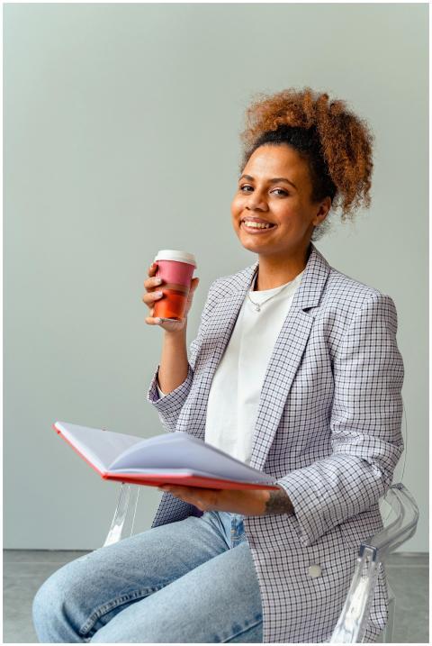 Smiling woman in blazer holds coffee cup and book,
