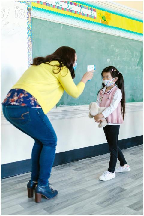 A teacher checks a student's temperature in a clas