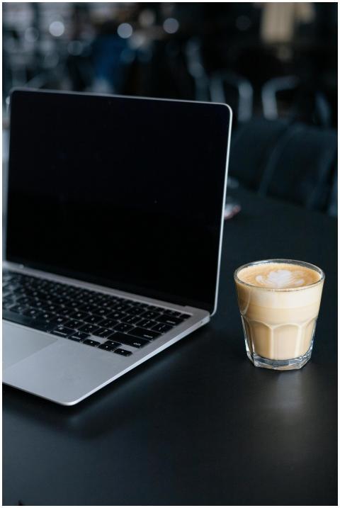 A sleek laptop and a latte on a dark tabletop, con
