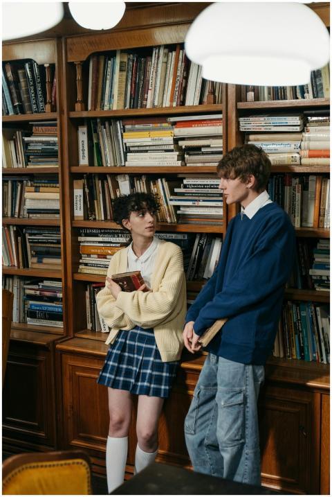 Two teenagers talking in front of a bookshelf in a