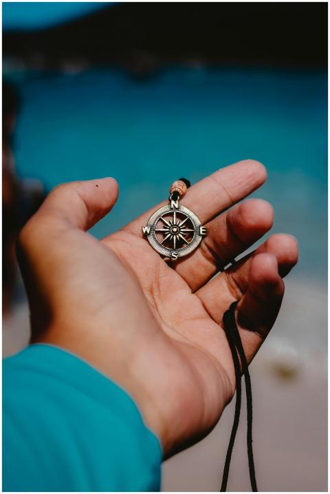 A hand holding a compass pendant with a blurred be