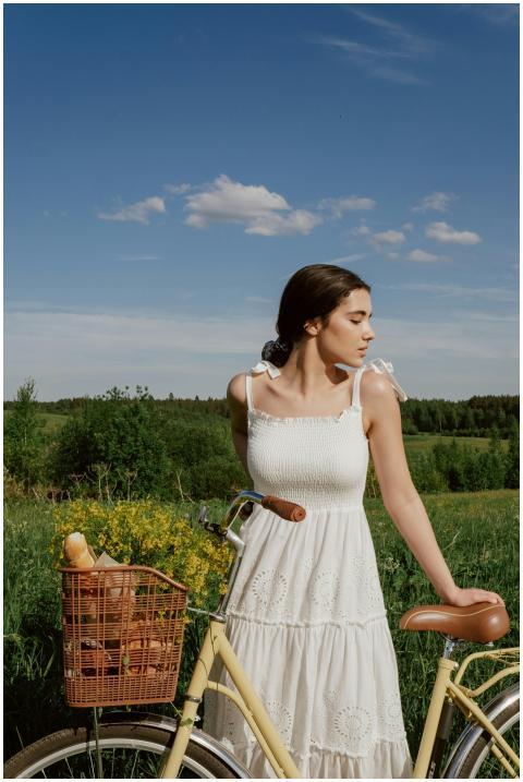 Woman in a white dress standing beside a bicycle w