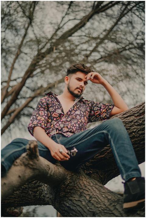 Stylish man in patterned shirt sits on a tree bran