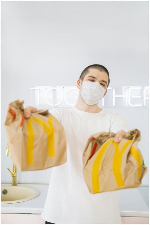 Man wearing a mask holds fast food bags indoors, e