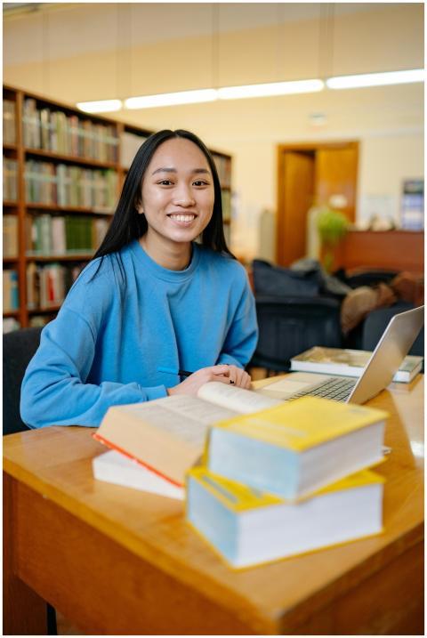A young woman student sitting in a library with bo