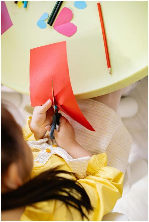 Top view of a girl cutting colored paper during a
