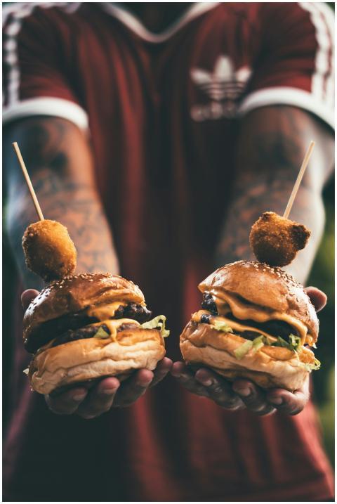 Two cheeseburgers held by a tattooed individual, s