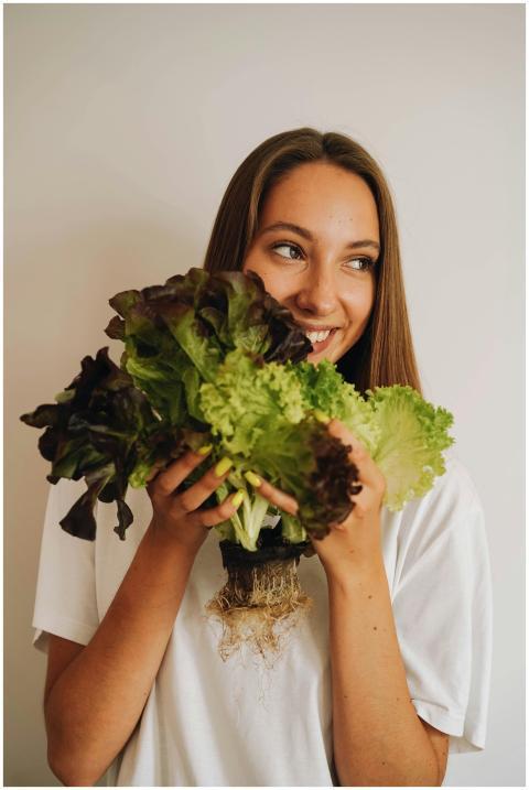 Happy woman holding fresh lettuce against a light