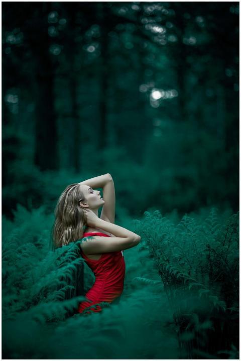 A woman poses in a vibrant red dress amidst lush g