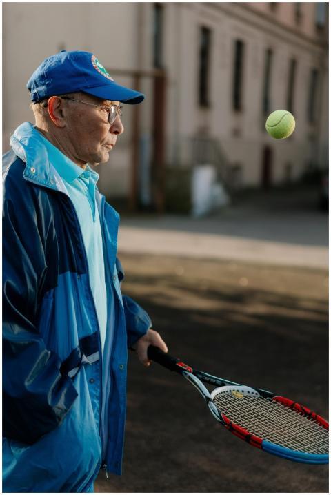 Elderly man in blue jacket playing tennis outdoors