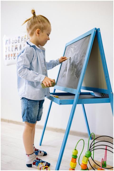 A young child writing on a blackboard in a bright