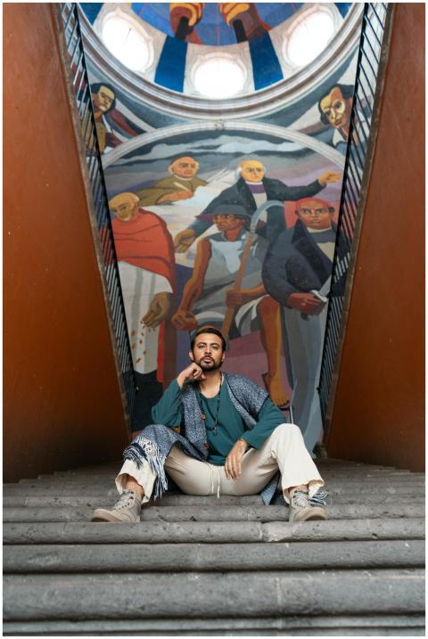 A man confidently sits on stairs in front of a col