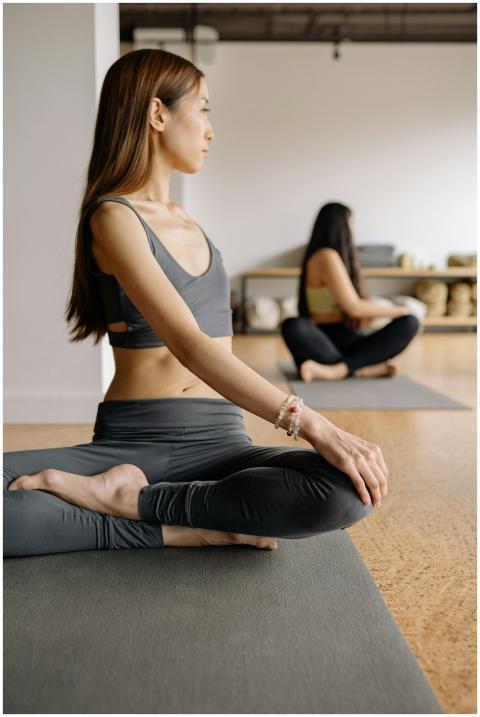 Two Asian women practicing yoga indoors, stretchin