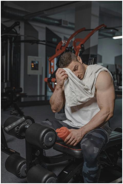 A muscular man in a gym resting and wiping sweat w