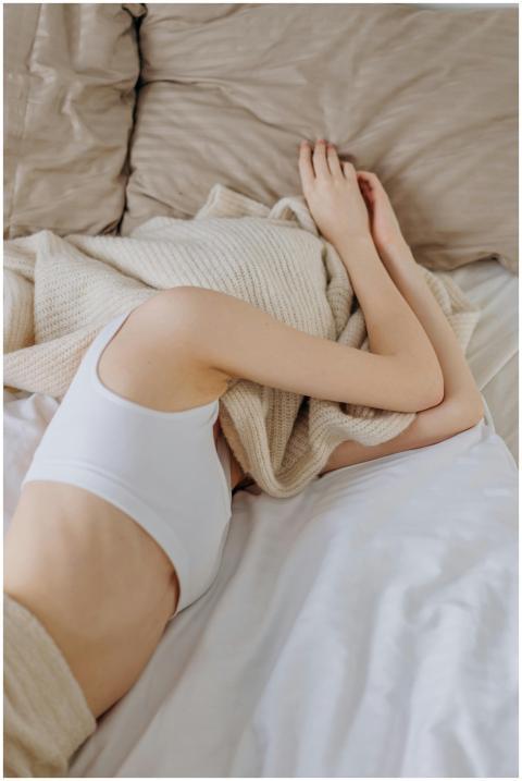 A woman peacefully resting in bed under a soft bei