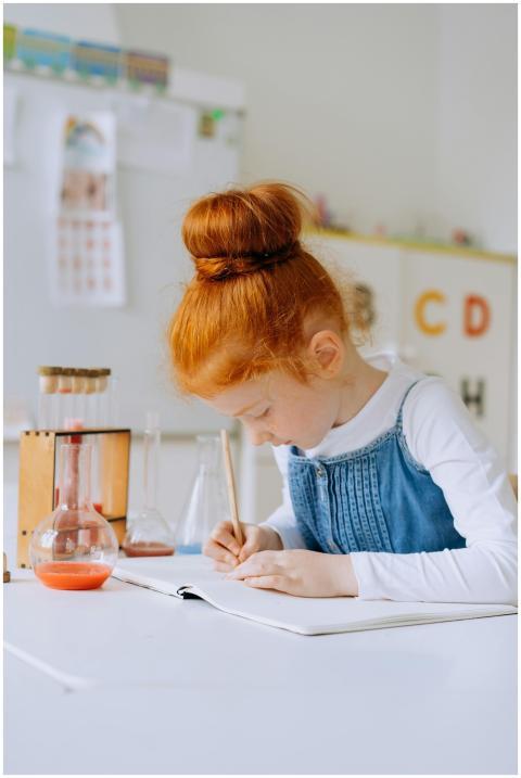 Red-haired girl writing in a notebook surrounded b